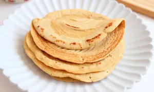 Pila di piadine di ceci dorate e leggermente maculate, servite su un piatto bianco a forma di fiore.