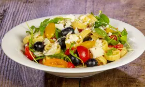 Pasta crudaiola colorata con pomodorini, olive nere, rucola e scaglie di parmigiano. Fresca e invitante.