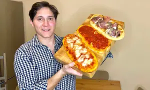 Uomo sorridente mostra tre lingue di pizza senza lievito: una margherita, una al pomodoro e una con prosciutto e funghi.