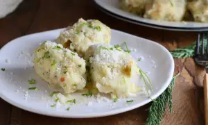 Tre gnocchi di pane soffici e dorati, cosparsi di parmigiano grattugiato e erba cipollina fresca, su un piatto bianco.