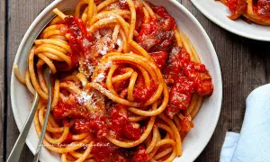 Un piatto di bucatini all'amatriciana ricetta, conditi con sugo rosso e guanciale croccante, spolverati di pecorino.