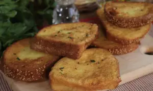 Fette dorate di pane fritto, cosparse di semi di sesamo e erbe aromatiche, pronte per essere gustate.