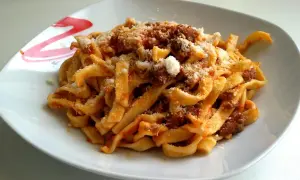 Un piatto invitante di tagliatelle al ragù, condite con abbondante parmigiano grattugiato.