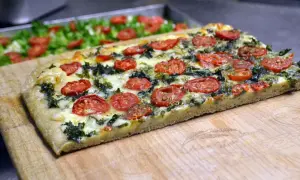 Focaccia messinese con pomodorini e verdure, un sapore autentico su un tagliere di legno.