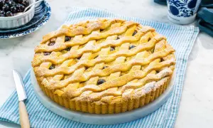 Una deliziosa crostata amalfitana con una griglia dorata di pasta frolla, cosparsa di zucchero a velo e ripiena di amarene.