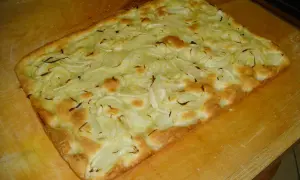 Focaccia con cipolle appena sfornata, dorata e fragrante, adagiata su un tagliere di legno.