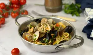 Un piatto di scialatielli ai frutti di mare, con cozze, vongole e pomodorini, guarnito con prezzemolo fresco.