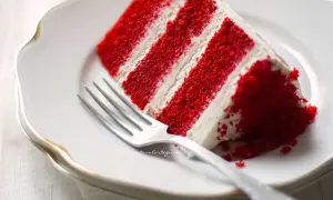 Una fetta di torta red velvet, stratificata con crema bianca, su un piatto bianco con una forchetta.