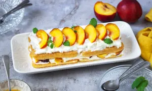 Delizioso tiramisù alle pesche, con strati di savoiardi, crema soffice e pesche fresche, guarnito con menta.