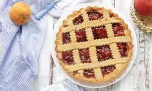 Deliziosa crostata di pesche con ripieno rosso brillante, decorata con strisce di pasta frolla a zig-zag.