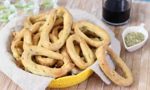 Taralli al finocchietto con lievito, croccanti e profumati, in un cestino con un bicchiere di vino rosso e semi di finocchio.