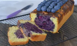 Plumcake ai mirtilli appena sfornato, con mirtilli freschi in cima e all'interno, su una griglia di raffreddamento.