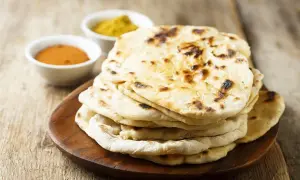 Pila di pane naan appena sfornato, con due ciotoline di spezie in sottofondo.