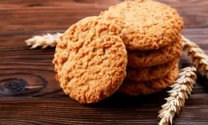 Biscotti integrali dorati e croccanti, impilati su un tavolo di legno scuro, con spighe di grano a decorare.