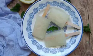Tre ghiaccioli al limone fatti in casa su un piatto decorato, con limone e menta fresca. Perfetti per un'estate rinfrescante.