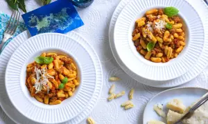 Due piatti di malloreddus alla campidanese, pasta sarda con sugo di salsiccia e pomodoro, guarniti con basilico e parmigiano.