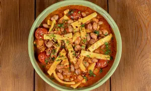 Piatto di sagne e fagioli fumante, con pomodorini e prezzemolo tritato, servito in una ciotola verde su un tavolo di legno.