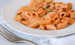 Piatto di penne alla vodka cremose, guarnite con erbe fresche, pronte per essere gustate con una forchetta.