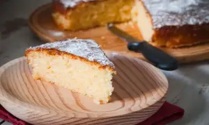 Una fetta di torta all'acqua soffice e spolverata di zucchero a velo su un piatto di legno.