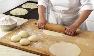 Mani esperte stendono la pasta per una piadina fatta in casa, mentre altre sono già pronte per essere cotte.