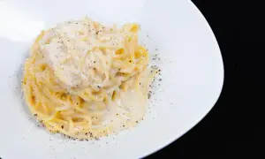 Pici cacio e pepe, un classico piatto di pasta romana, servito su un piatto bianco con abbondante pepe nero macinato e formaggio grattugiato.