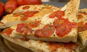 Focaccia barese soffice e dorata, condita con pomodorini freschi e origano, pronta per essere gustata.