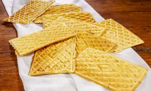 Un mucchio di croccanti ferratelle abruzzesi, dolci tradizionali dorati, disposte su un panno bianco su un tavolo di legno.