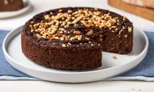 Torta paesana al cioccolato, ricca e umida, guarnita con pinoli tostati. Una fetta è stata già servita, invitando a gustare questo dolce rustico.