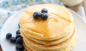 Pancakes senza glutine dorati, impilati e guarniti con mirtilli freschi e sciroppo d'acero.