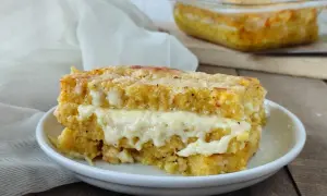 Una fetta di pasticcio di polenta con formaggio filante, cotto al forno e servito su un piatto bianco.