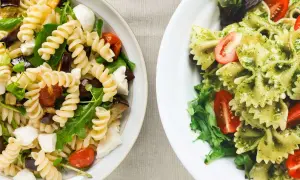 Due insalate di pasta fredda senza pomodori: una con fusilli, melanzane e mozzarella, l'altra con farfalle al pesto e pomodorini.