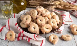 Un piatto colmo di taralli al vino bianco, cosparsi di zucchero, accanto a un bicchiere di vino e una bottiglia d'olio.