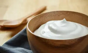 Una ciotola di legno piena di soffice crema di latte, perfetta per la tua prossima ricetta. Due cucchiai di legno sullo sfondo.