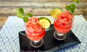 Due bicchieri di granita di anguria, guarniti con fettine di lime e foglie di menta, su un vassoio nero.