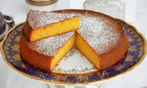 Una deliziosa torta carote e mandorle, spolverata di zucchero a velo, servita su un elegante piatto blu e oro.