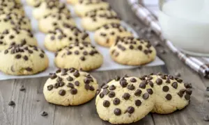 Biscotti con gocce di cioccolato, dorati e invitanti, sparsi su un tavolo di legno. Alcuni sono in primo piano, altri sullo sfondo.