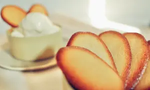 Biscotti croccanti a forma di lingue di gatto, alcuni in primo piano, altri decorano una coppa di panna montata.