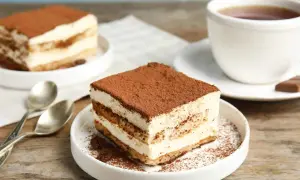 Delizioso tiramisù, perfetto per la tua tiramisù ricetta benedetta. Servito su un piatto bianco con caffè e cucchiaini.