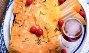 Pane guttiau croccante con pomodorini, rosmarino e fette di formaggio, accompagnato da un bicchiere di vino rosso.