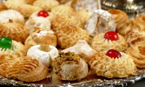 Vassoio pieno di dolcetti invitanti, tra cui spiccano le paste di mandorla decorate con ciliegie candite e granella di pistacchio.