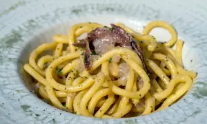 Un piatto di bigoli in salsa, con pasta spessa e condimento saporito, guarnito con prezzemolo tritato.