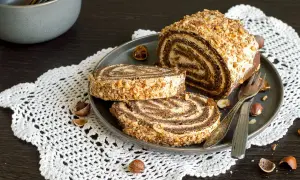 Un delizioso rotolo alla Nutella, ricoperto di granella di nocciole, servito su un piatto con due fette tagliate.