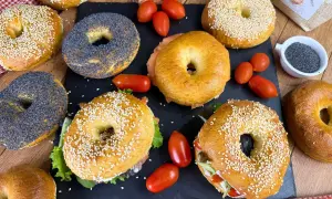 Varietà di bagel, alcuni con semi di sesamo, altri con semi di papavero, pronti per una deliziosa bagel ricetta. Pomodorini e salmone completano la scena.