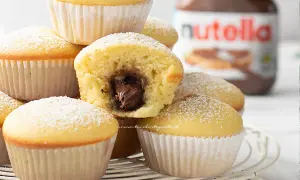 Muffin soffici con cuore di Nutella, perfetti per chi ama le ricette dolci. Un vasetto di Nutella sullo sfondo.
