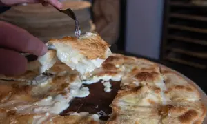 Una fetta di focaccia di Recco ricetta, filante e dorata, viene sollevata con una forchetta.