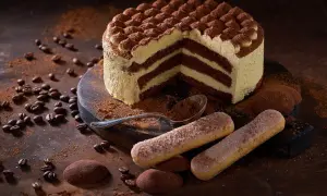 Una fetta di torta tiramisù, con strati di crema e cacao, circondata da savoiardi, chicchi di caffè e cacao in polvere.