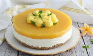 Cheesecake al mango con palline di frutta e menta fresca, su una base croccante. Un dolce estivo invitante.