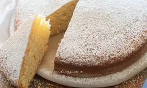 Una soffice torta senza uova, cosparsa di zucchero a velo, con una fetta tagliata che ne mostra l'interno chiaro e profumato.