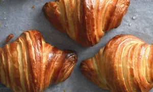 Cornetti dorati e sfogliati, perfetti per la ricetta cornetti fatti in casa. Si intravedono gocce d'acqua sulla carta da forno.