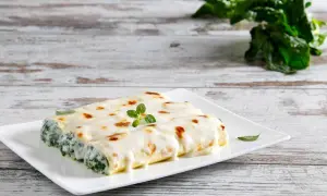 Cannelloni ricotta e spinaci gratinati, serviti su un piatto bianco con una guarnizione di origano fresco.